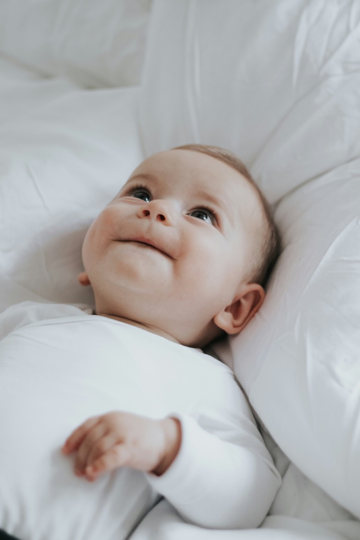 A baby lying awake and content in white bedding, looking up
